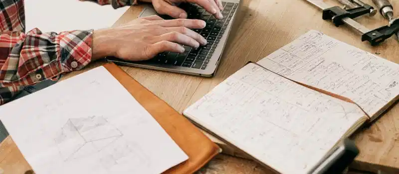 A woodworker uses a laptop to design furniture in a workshop setting, highlighting the blend of technology and craftsmanship.