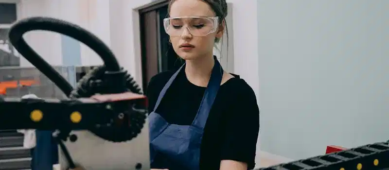 A female engineer operates machinery with precision in an industrial setting, wearing safety glasses.