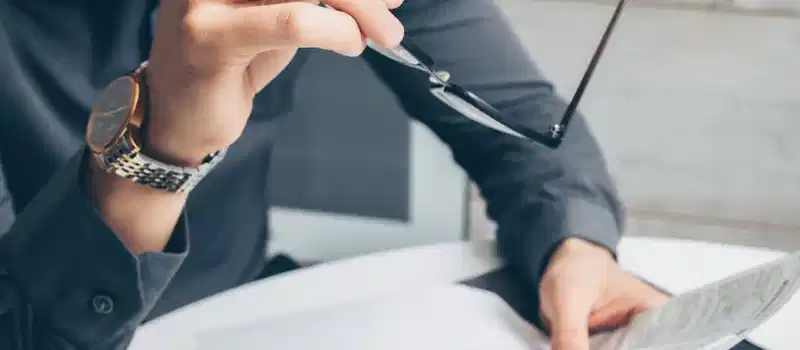 Man in formal attire reviewing paperwork, holding glasses. Business setting.