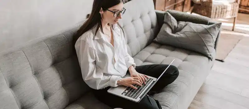 Woman in a cozy home setting working on a laptop for remote work and relaxation.