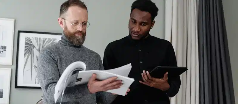 Two businessmen analyzing documents and using a tablet in a modern office setting.