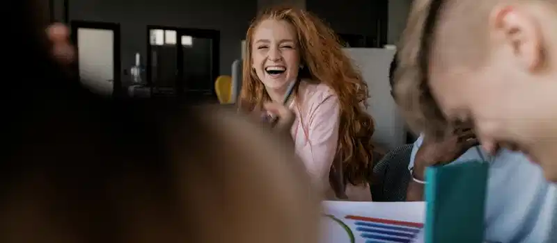 Joyful red-haired woman laughing during a casual meeting indoors.