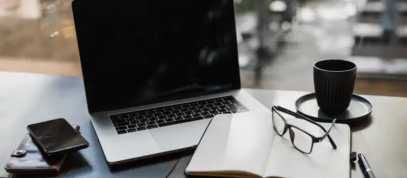 Workspace setup featuring a laptop, notepad, glasses, and coffee cup for productivity.