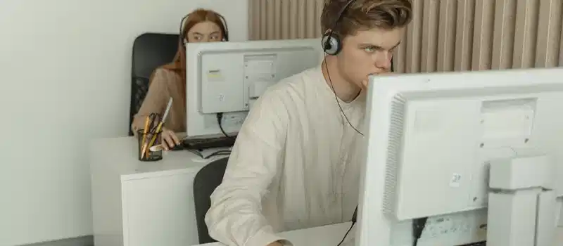 Two young professionals working diligently on computers in a modern office setting.