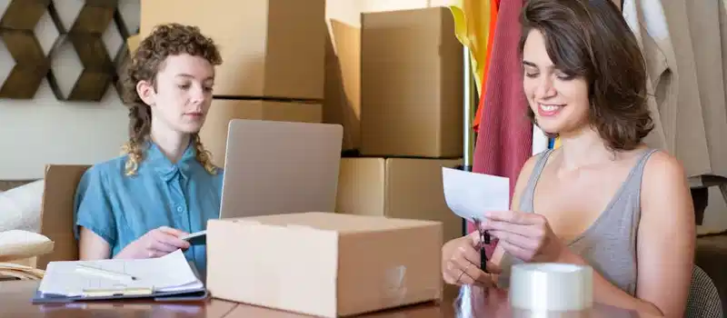 Two women organizing and managing an online clothing store with boxes and a laptop.