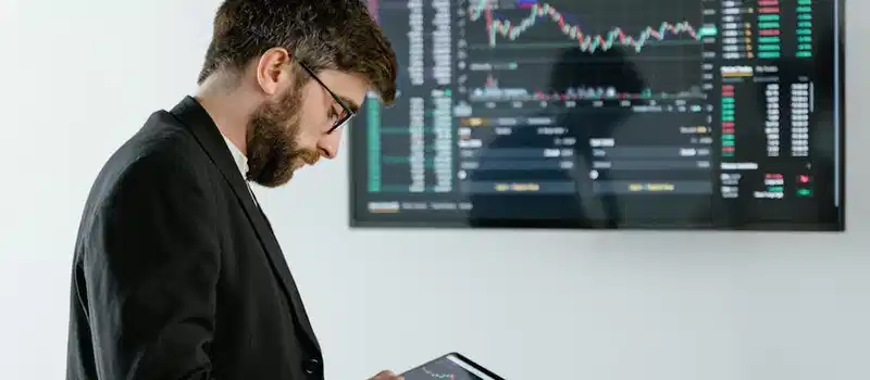 Professional man using tablet in front of cryptocurrency trading screen indoors.