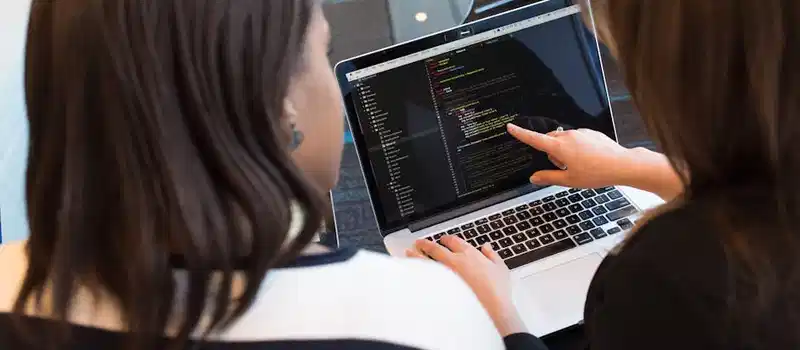 Two women working together on software programming indoors, focusing on code.