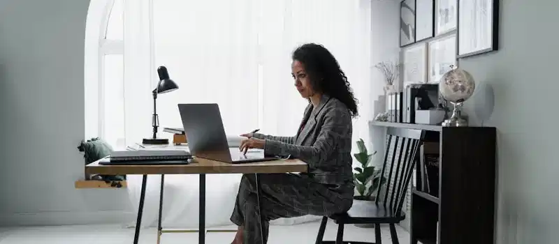 Businesswoman using a laptop at a stylish desk, focused on work in a modern office environment.