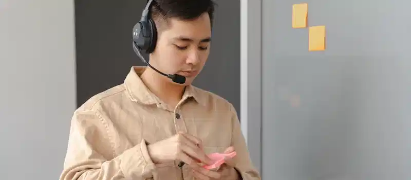 Young adult in an office setting using a headset and sticky notes. Ideal for business communication visuals.