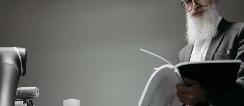 Elderly man reads as a robotic arm holds a coffee cup, showcasing technology integration.