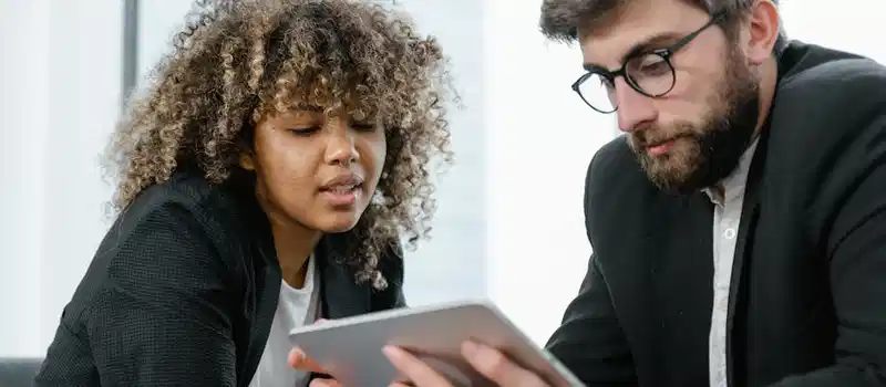 Two business professionals reviewing data on a tablet, fostering collaboration and teamwork in a modern office setting.