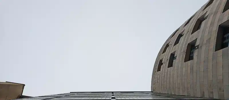 Looking up at a modern glass and stone building facade against a clear sky.