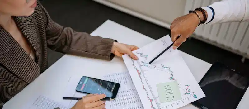 Two professionals analyzing stock market data and graphs at a desk.