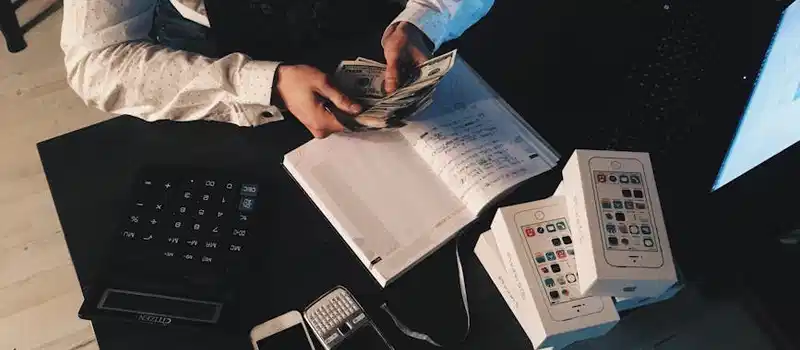 Businessman organizing finances with tech devices and cash on desk.