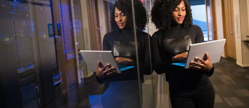 African American woman standing in modern office using laptop, reflecting professionalism and technology engagement.