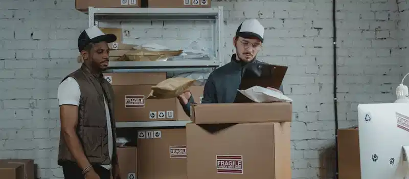 Two workers in a warehouse handling and checking fragile labeled packages before shipping.