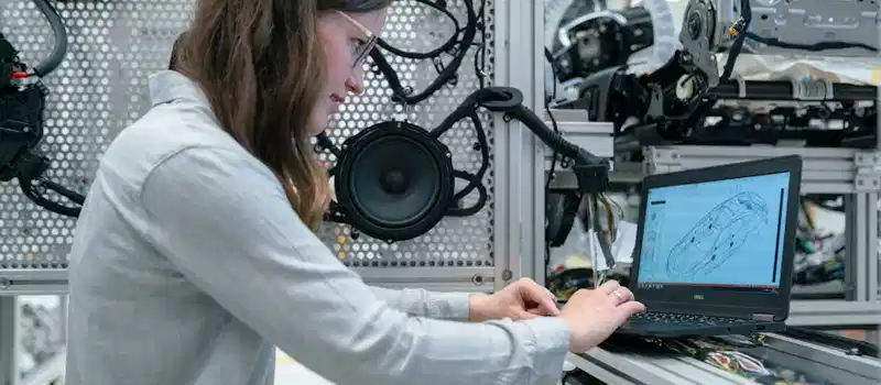 Woman conducting engineering research in a sound system workshop using a laptop.