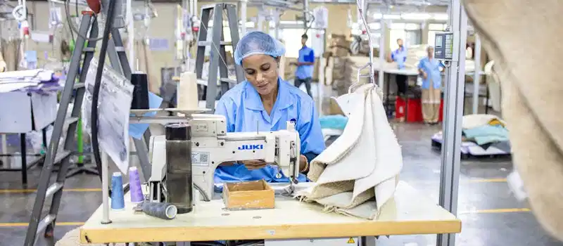 Textile factory worker sewing fabric using Juki machine in industrial setting.