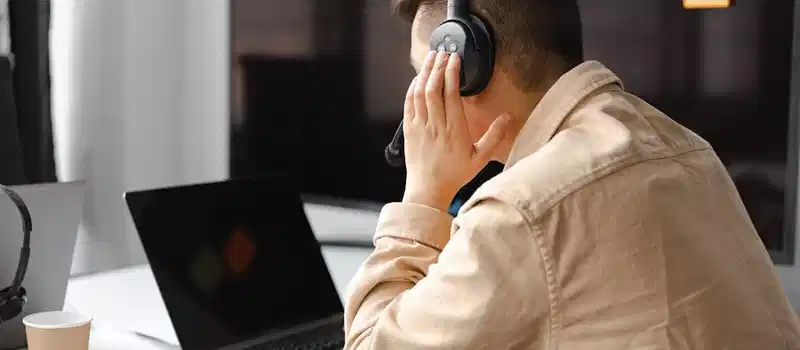 A man wearing headphones works at a laptop in a modern office setting.