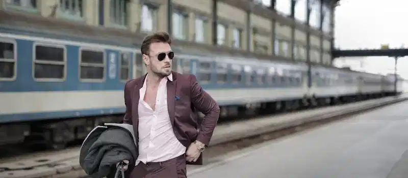 A fashionable man in sunglasses and suit waiting at an urban train station. Perfect for business-related themes.