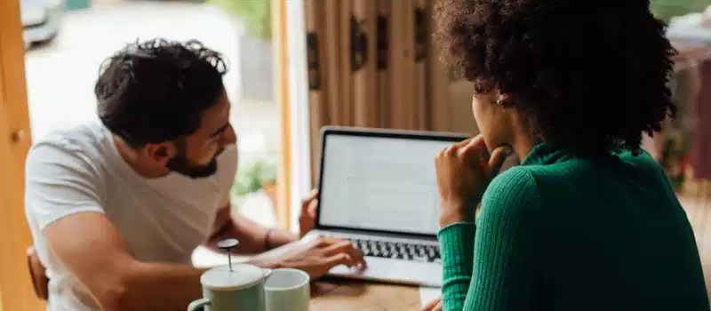 Two adults discussing work at home, using a laptop and enjoying coffee.