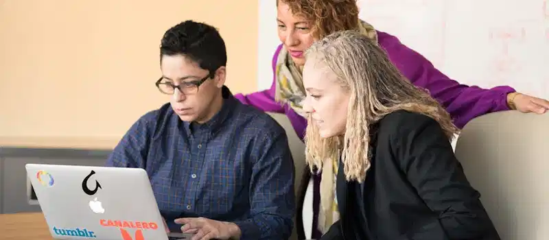 Team of three people collaborating on a laptop in an office setting.