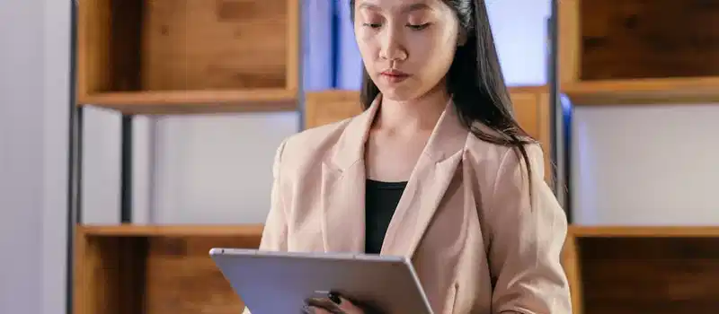 Young Asian businesswoman using a tablet in a modern office setting.