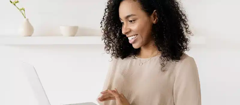 Smiling woman working on a laptop in a modern home office, highlighting freelance lifestyle.