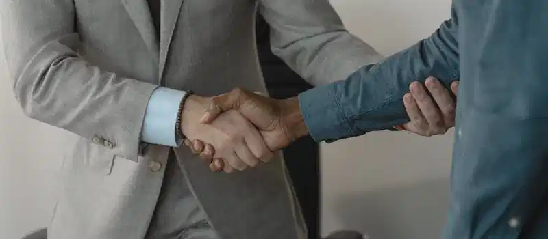 Image of a professional handshake between two businessmen in an office setting.