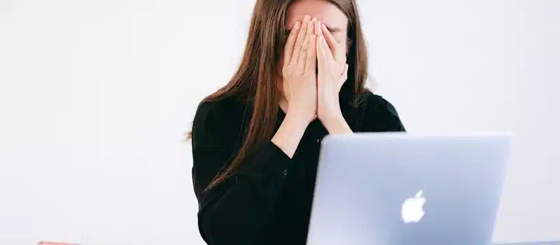 Woman feeling stressed and overwhelmed at her desk while working remotely on a laptop.