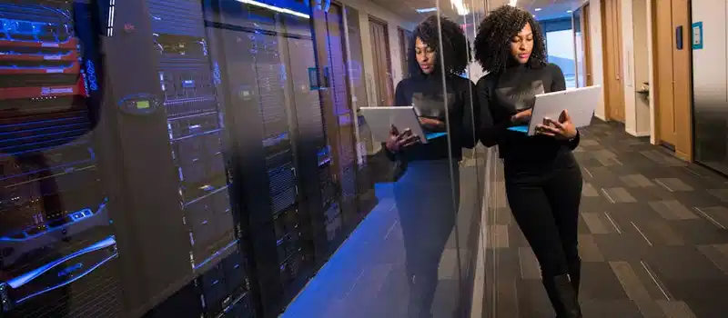 A woman using a laptop navigating a contemporary data center with mirrored servers.