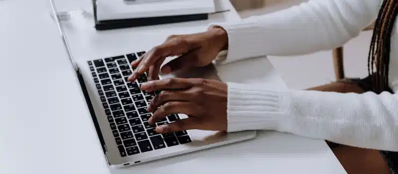 Close-up of woman's hands typing on a laptop in a modern home office setting.