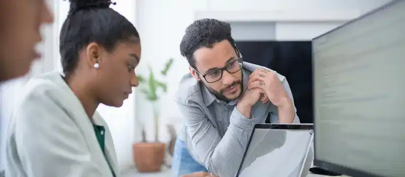 Two people collaborate in a modern office setting, focused on computer work