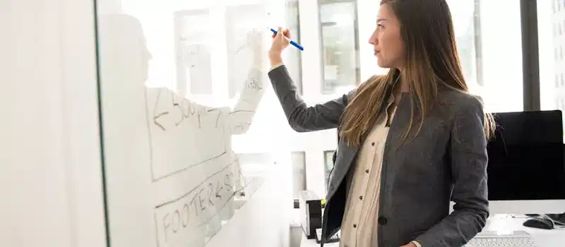 Professional woman writing on a whiteboard in an office environment, focusing on ideas.