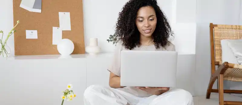 Young woman with curly hair working on her laptop in a cozy home setting, exuding confidence and focus.