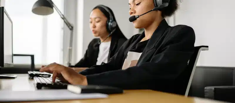 Two call center agents working at desks in an office setting with headsets.