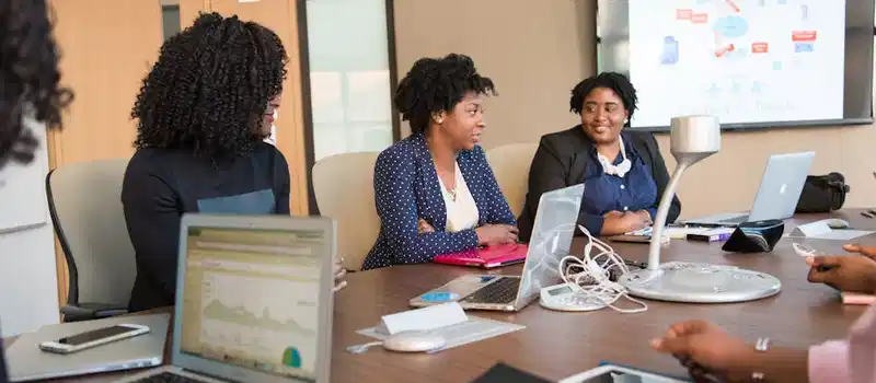 Four diverse women engaged in a business meeting with laptops and presentations in an office.