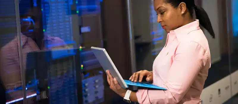 A focused software engineer working on a laptop in a server room, reflecting dedication in tech.