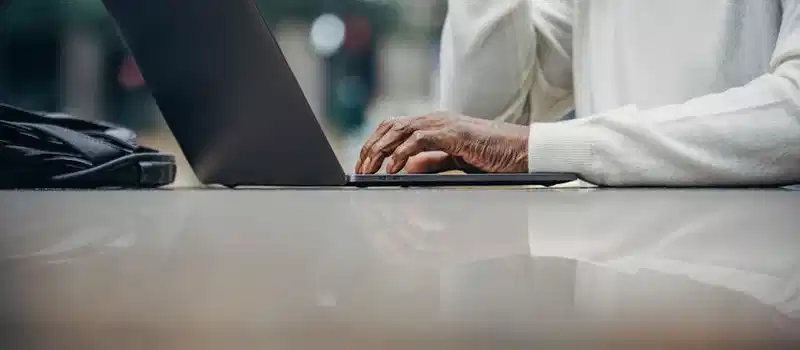 Low angle of crop anonymous mature black male freelancer typing on laptop keyboard while working remotely in outdoor cafe