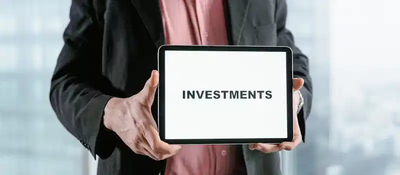 Professional holding a tablet with 'INVESTMENTS' text, ideal for finance and business themes.
