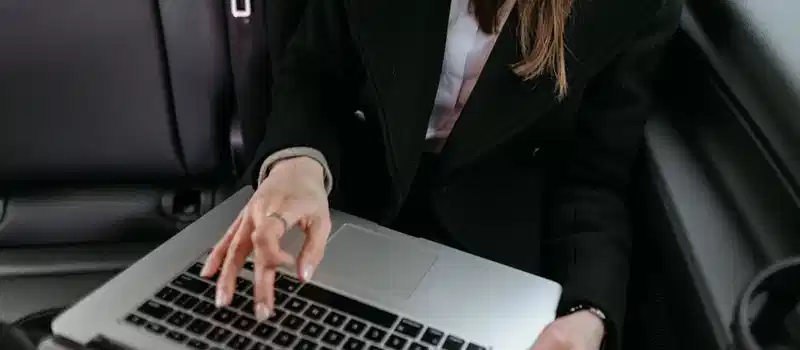 Businesswoman in black blazer using laptop inside a car, focused on work.