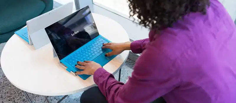 A woman typing on a laptop at a round table in a modern indoor setting.