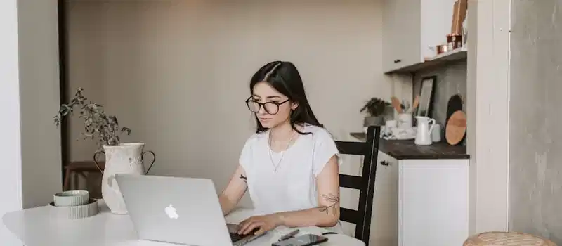 Young woman using a laptop in a stylish home office setting, focusing on remote work tasks.