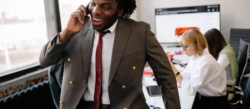 A professional businessman in a suit on a phone call in a busy office environment.
