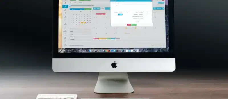 A sleek office setup featuring an Apple iMac, iPad, and keyboard on a wooden desk.