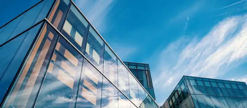 Low angle view of contemporary glass office buildings reflecting a vibrant blue sky.