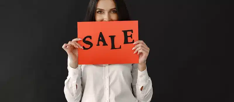 Woman in white shirt holding a red sale sign against a black backdrop. Ideal for advertising.