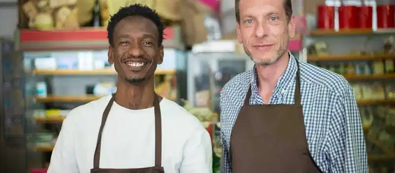 Two happy store owners smiling while wearing aprons in a local grocery store.
