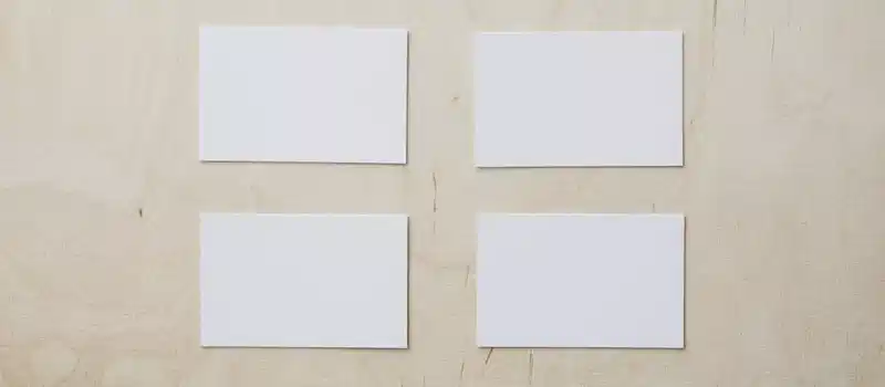 Overhead view of clean white mockup greeting cards placed on light brown wooden desk