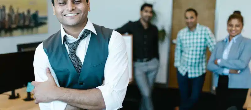 Smiling businessman in a vest with diverse team posing in modern office setting.